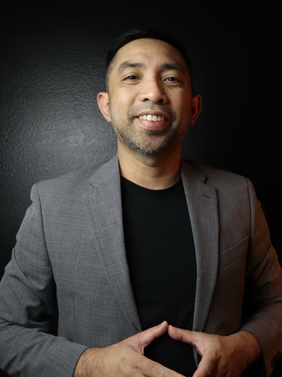 JP Galido, smiling warmly in a gray blazer against a dark background.
